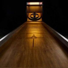 a long wooden bowling alley with a light on it's side and an arrow painted on the floor