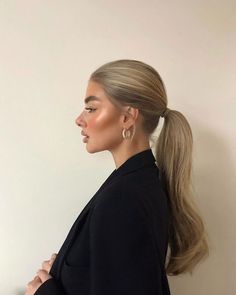 a woman with long blonde hair in a ponytail wearing a black blazer and earrings