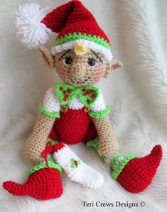 a crocheted elf doll sitting on top of a white blanket with a green and red hat