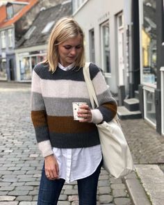 a woman is walking down the street looking at her cell phone and holding a bag