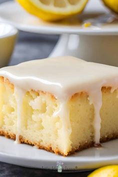 a slice of lemon cake with icing on a plate next to some lemons