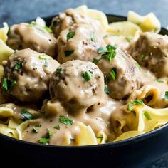 a bowl filled with pasta and meatballs covered in gravy, garnished with parsley