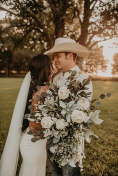 a bride and groom are standing in the grass with their arms around each other as they kiss