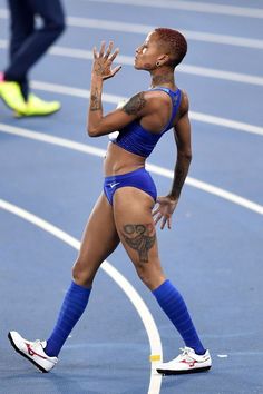 a woman with tattoos on her body standing on a track in a blue sports suit