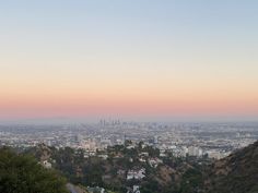 a view of the city from atop a hill with trees and hills in the foreground