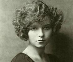 an old black and white photo of a woman with curly hair wearing a brown dress