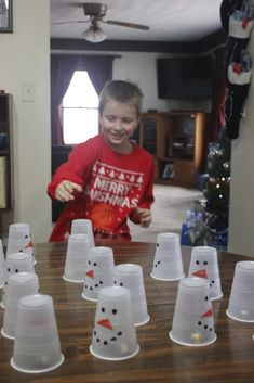 a young boy standing in front of a wooden table with white cups on top of it