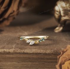 a gold ring with green and white stones sits on top of a wooden table next to a book