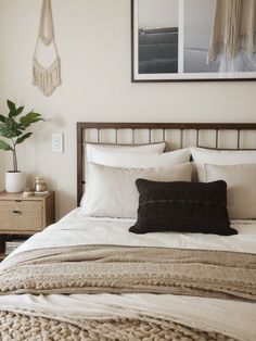 a bed with white linens and pillows in a bedroom next to a potted plant