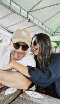 a man and woman sitting at a picnic table smiling for the camera with their arms around each other