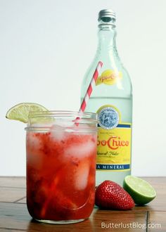 a drink with strawberries and lime next to a bottle