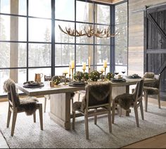 a dining room table with chairs, candles and deer antlers hanging from the ceiling