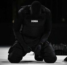 a man kneeling down in front of a black object with the word donda written on it