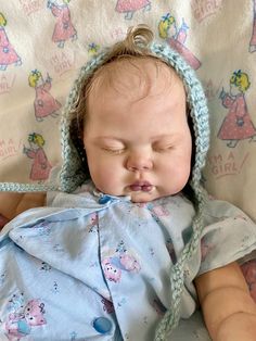 a baby is laying down wearing a blue bonnet and sleeping with its eyes closed on a blanket