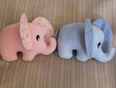 two stuffed elephants laying next to each other on top of a bed, one pink and the other blue