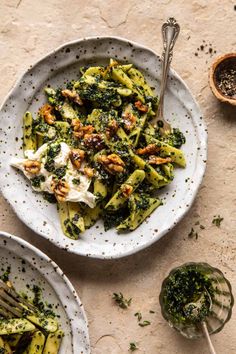 two white plates filled with pasta and broccoli covered in pesto on top of a table