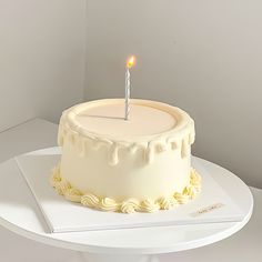 a white cake with a single lit candle on it