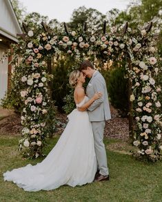 a bride and groom kissing in front of an outdoor wedding arch with flowers on it