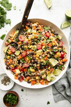 a white bowl filled with black beans, corn and avocado salad next to cilantro