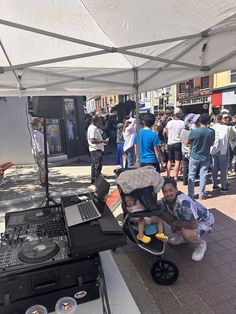 a baby in a stroller sitting next to an outdoor dj's set up