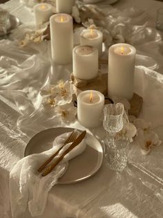 a table topped with white candles and plates