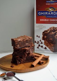 two pieces of brownie on a wooden plate next to a box of ghirardden's chocolate