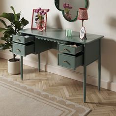 a green desk with two drawers and a mirror on the wall next to a potted plant