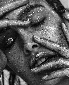 a black and white photo of a woman with glitter on her face holding her hands to her eyes