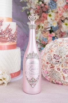 a pink bottle sitting next to a wedding cake on top of a table with flowers