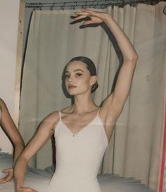 a woman in a white leotard stretching her arms up with one hand above her head