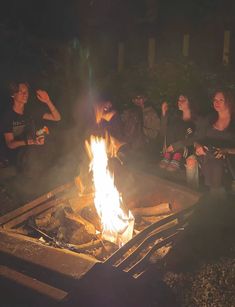 people sitting around a fire pit at night with their hands in the air and looking on