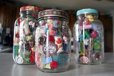 three glass jars filled with assorted buttons and magnets sitting on a counter top