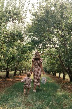 a woman and child walking through an apple orchard