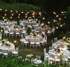 an outdoor wedding reception set up with white linens and chairs, lit by fairy lights