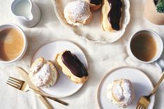 two plates with pastries on them next to cups of coffee and spoons,