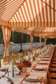 an outdoor dining area with orange and white striped tented tables set up for dinner