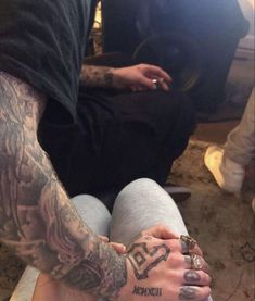 a man with tattoos on his arm and leg sitting next to a woman's foot