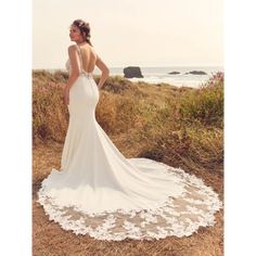 a woman in a wedding dress is standing on the beach looking at the ocean with her back to the camera