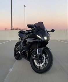 a black motorcycle is driving down the road at sunset or dawn with its headlights on