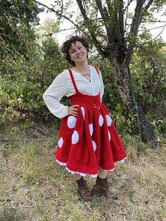 a woman wearing a red and white dress standing in front of a tree with her hands on her hips