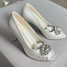 a pair of white high heeled shoes sitting on top of a gray ottoman