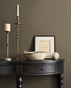 a wooden table with a bowl and candles on it next to a framed photograph, candle holder and other items