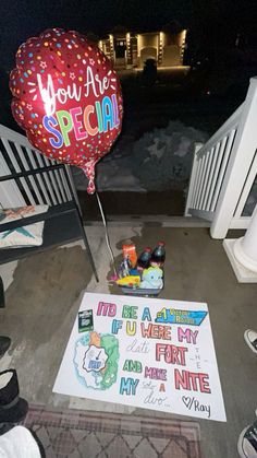 a sign and balloons on the ground near some white railings at night with lights in the background