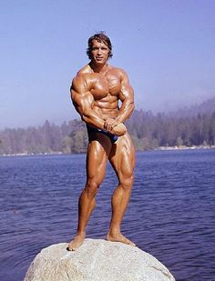 a man standing on top of a large rock next to the water with his hands in his pockets