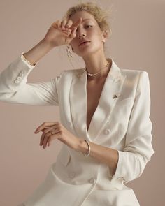 a woman in a white suit is posing with her hand on her head and wearing a necklace