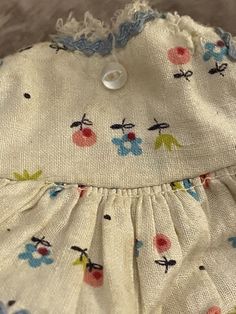 a white dress with blue and pink flowers on it's chest, sitting on a bed