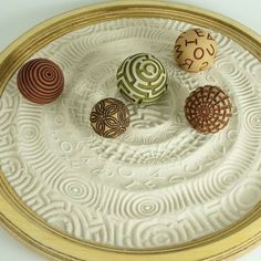 four ceramic balls sitting on top of a white plate with gold trimmings and swirl designs