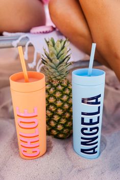 two different colored cups sitting next to each other on a bed with a pineapple in the background