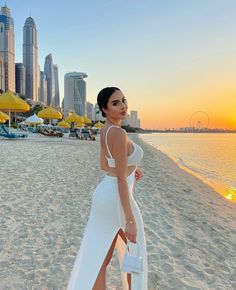 a woman standing on top of a sandy beach next to the ocean and tall buildings