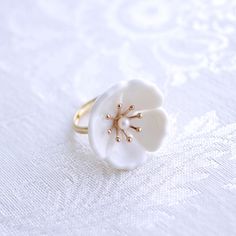 The beautiful plum blossom, who never fears frost and snow, bravely flowers in the coldest seasons, awakening spring and bringing hope. The pure and delicate petals deserve your extra love and care. Ring is made of porcelain flower; gold-plated silver ring and a small freshwater pearl. Material: Handmade porcelain plum blossom; Gold-plated silver ring; Small freshwater pearl. Gold- or silver-plated colour will fade over time. This is a normal result from long-term wear and contact with air. Howe Delicate White Flower-shaped Ring, Delicate White Flower Ring, Delicate White Flower Shaped Ring, Delicate White Flower Ring For Wedding, White Flower Shaped Anniversary Ring, Nature-inspired White Flower Ring, White Plum, Handmade Porcelain, Porcelain Jewelry